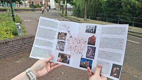 Iemand leest de folder van de Stadswandeling met op de achtergrond de Westsingel.