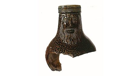 Een deel van een kruik met daaroop een gezicht van iemand met baard.