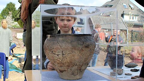Een kind dat kijkt naar een kruik in een kleine vitrine.
