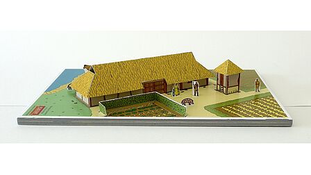 Een bouwplaat van karton van een maquette van een boerderij uit de Middeleeuwen.